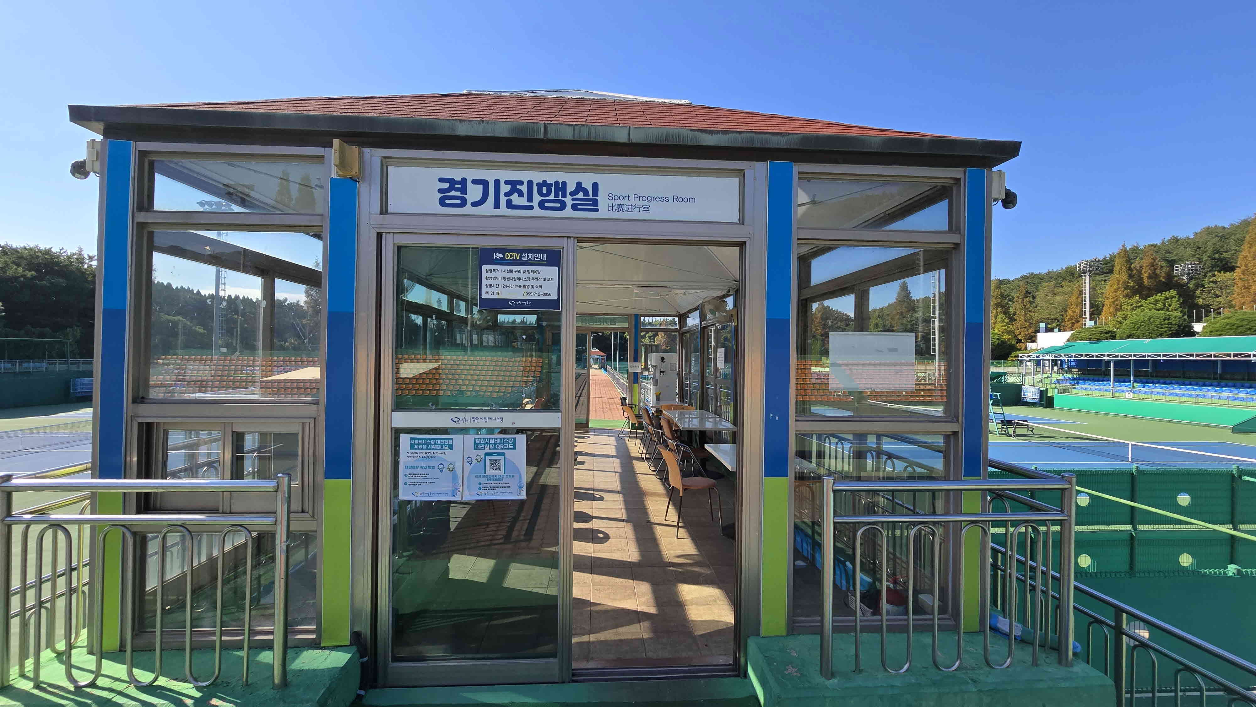 보조경기장 사이에 위치한 경기진행실 외관 전경을 담은 사진이며, 회원분들이 경기 진행상황을 보고 휴식공간을 취할 수 있는 테이블 및 좌석이 배치되어 있습니다.