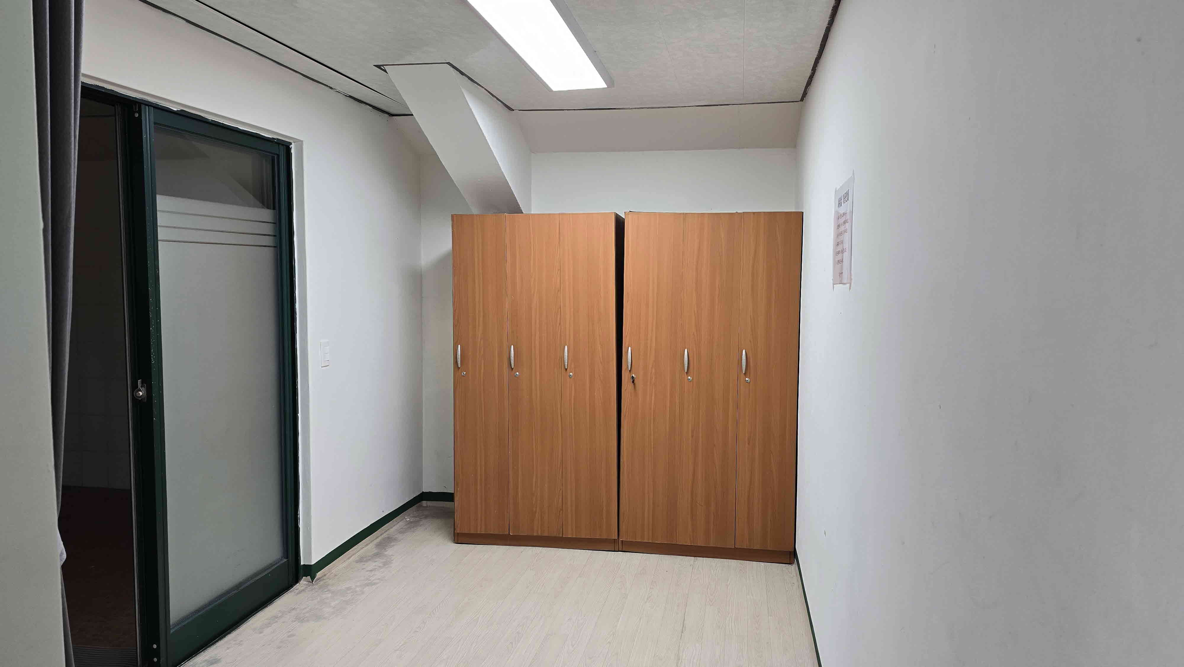 샤워실 옆 탈의실 내부 사진이며, 좌측에는 샤워실 입구와 목재 캐비닛 6개가 비치되어 있습니다.