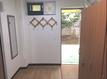 출입구 방면으로 촬영한 샤워실 옆 탈의실 내부이며, 목재 캐비닛과 거울, 옷걸이가 비치되어 있습니다.