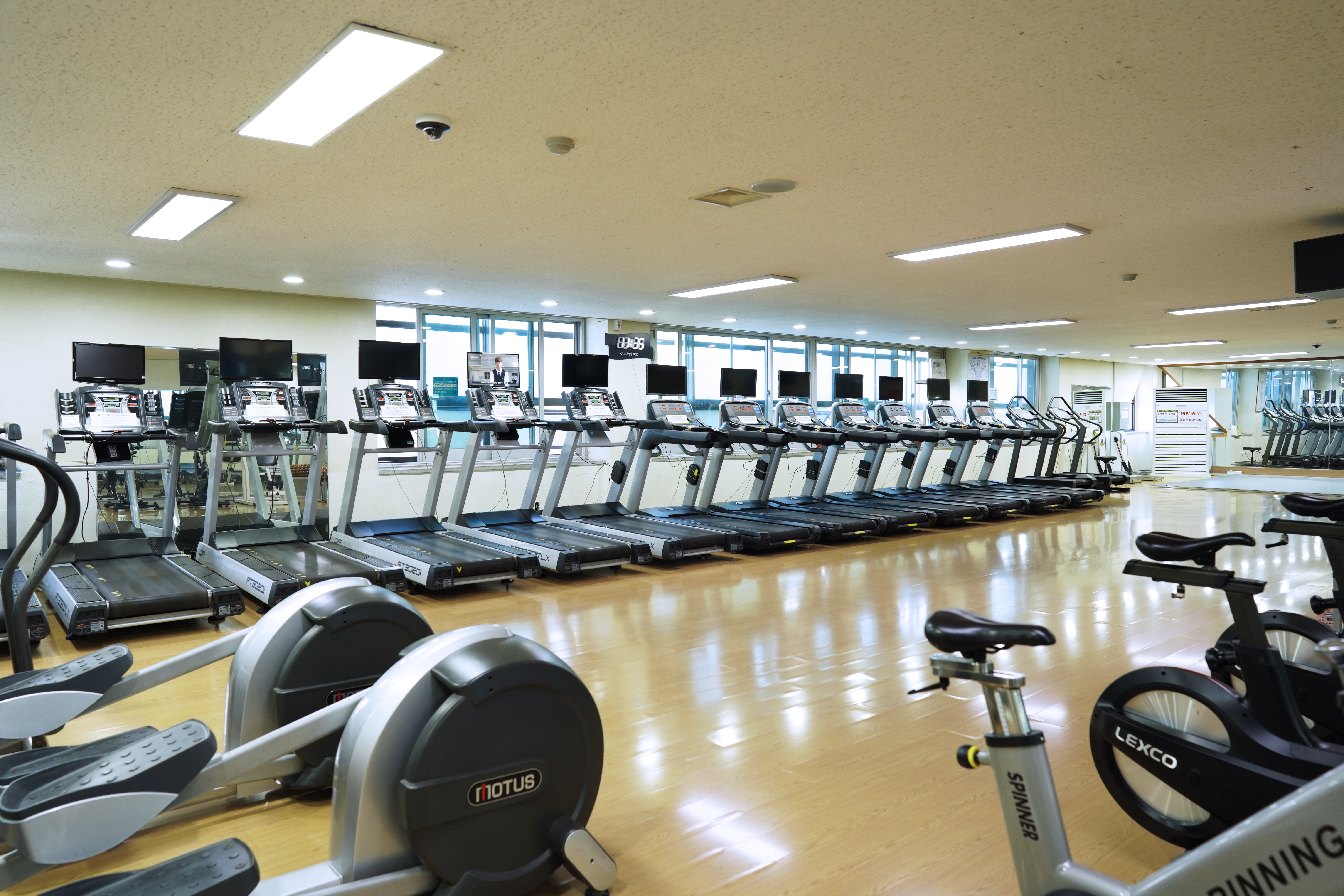 창원실내수영장 2층 유산소실을 정면에서 촬영하여 러닝머신과 사이클 기구가 정렬된 배치와 넓고 쾌적한 실내 환경을 담은 사진입니다.