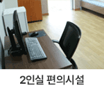 2인실 편의시설 : 창원축구센터 숙소 2인실 편의시설을 찍은 사진입니다. 책상 위에 데스크톱 컴퓨터가 배치되어 있으며 안쪽으로는 냉장고와 캐비닛이 위치하고 있습니다. 뒤편으로는 창문이 있어 채광이 들어오고 있는 사진입니다.