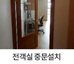 전객실 중문설치 : 객실 중문 사진입니다. 방 입구는 나무 문으로 되어 있고, 안쪽에는 의자가 놓여 있는 책상이 보입니다.