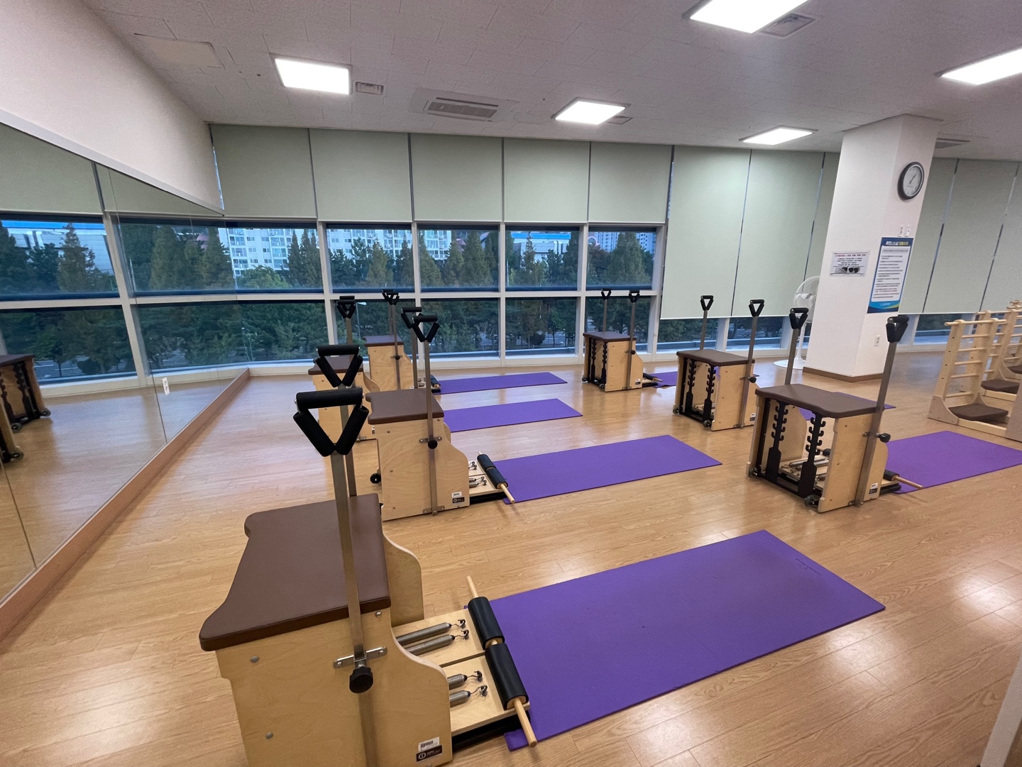 입구 쪽에서 바라본 성산스포츠센터 휘트니스4실 기구필라테스실 내부 사진이며 기구 필라테스 중 하체 근력 및 골반 교정 효과가 큰 앞뒤가 뚫려있고 손잡이가 있는 체어 기구가 일렬로 나열되어 있으며, 각 기구 옆에는 매트가 깔려있습니다.
