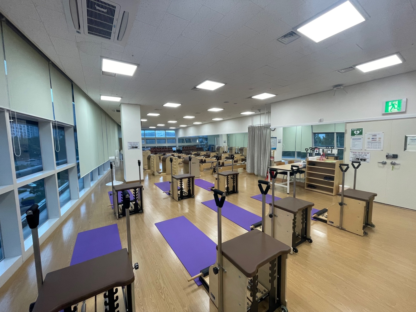 정면에서 바라본 성산스포츠센터 휘트니스4실 기구 필라테스실에 체어 기구 7대가 나열되어 있으며, 각 기구 옆에는 매트가 깔려있습니다. 입구 우측에는 신발장과 책상이 위치해 있습니다.