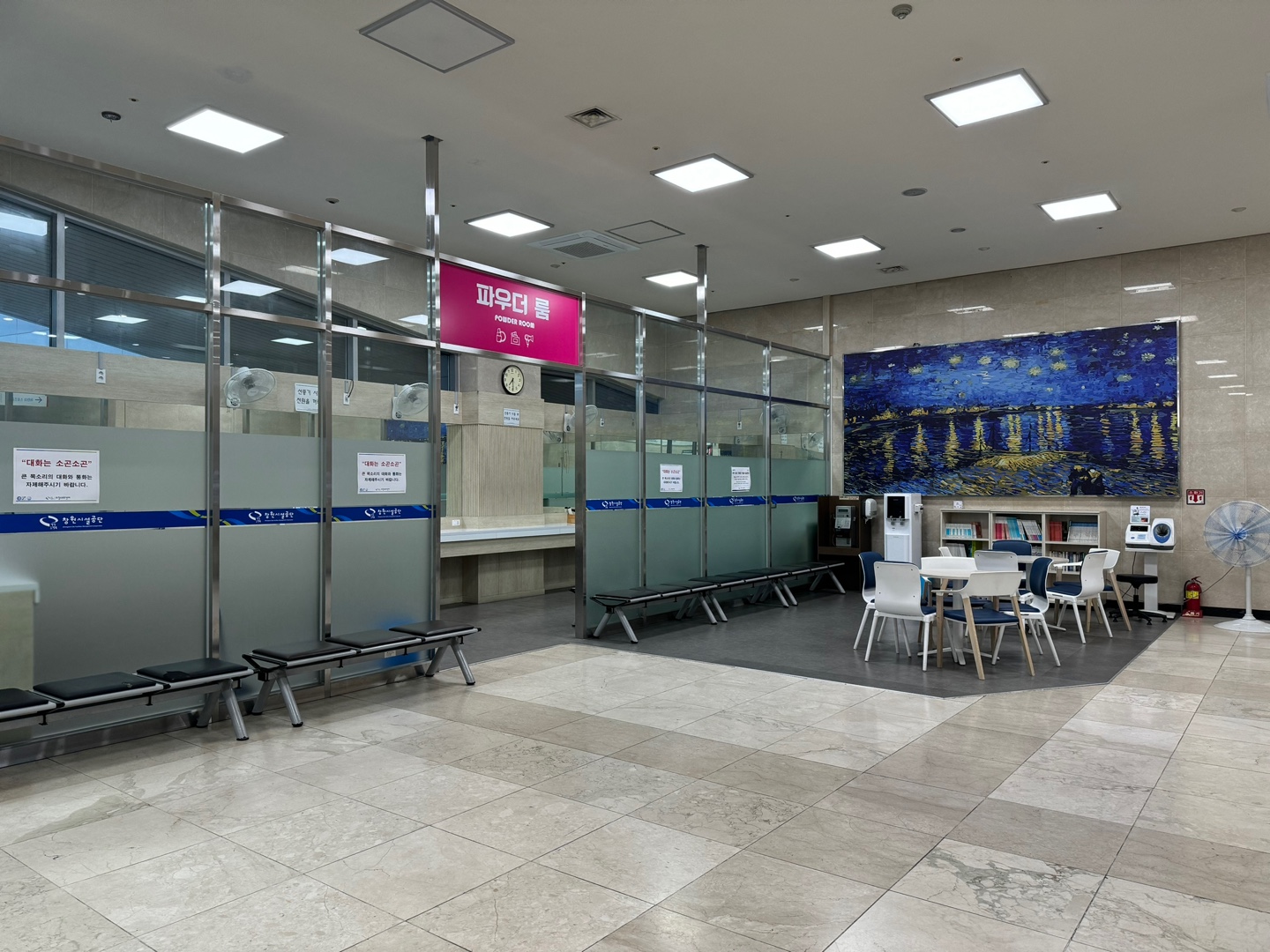 파우더룸 입구를 촬영한 사진이며, 입구 앞에는 혈압측정기, 정수기, 책 등과 함께 앉을 수 있는 휴식공간이 마련되어 있습니다.