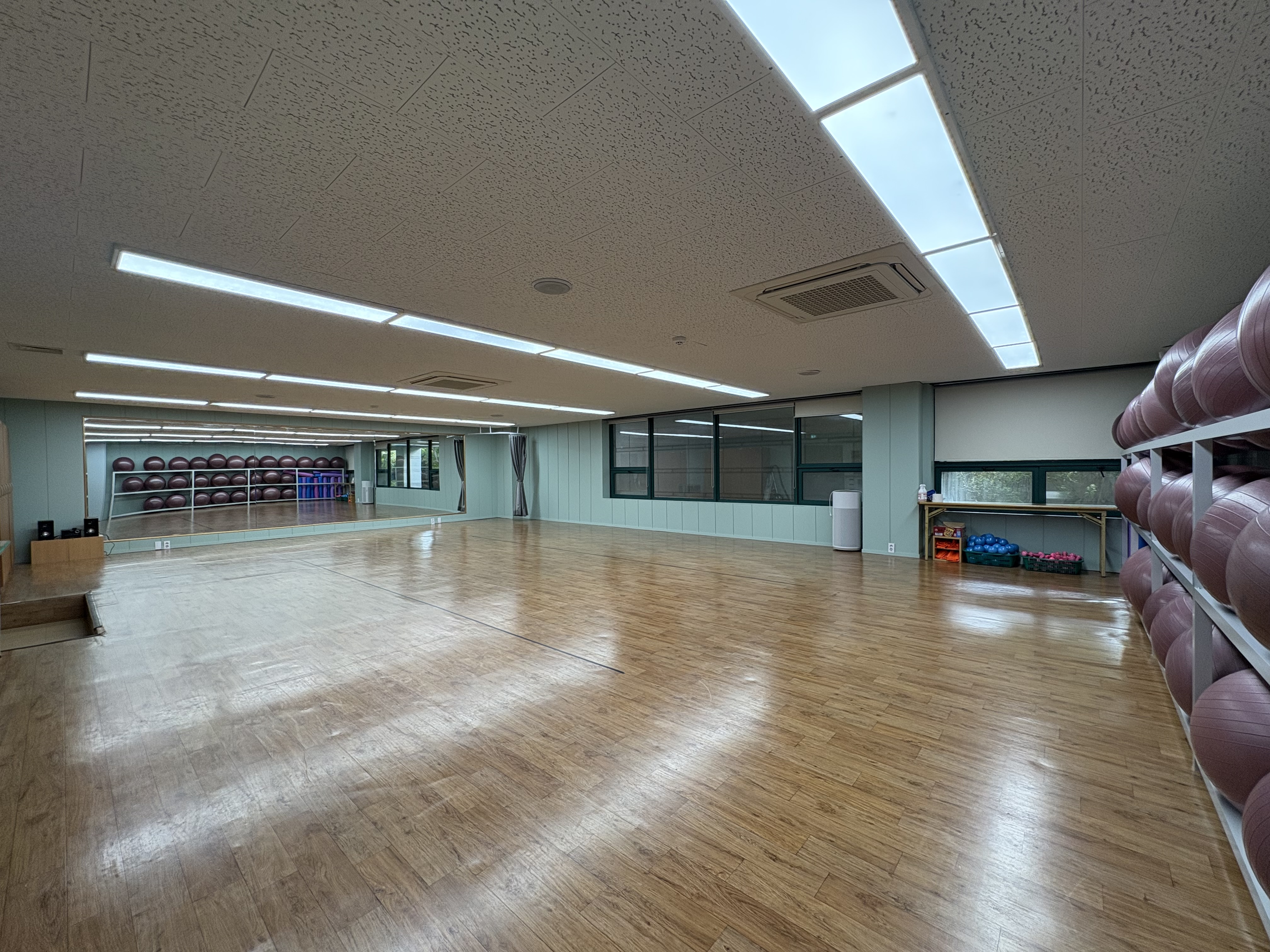 요가실 뒤 가장자리에서 전체를 촬영한 사진입니다. 마루 바닥과 전면 거울이 보입니다.