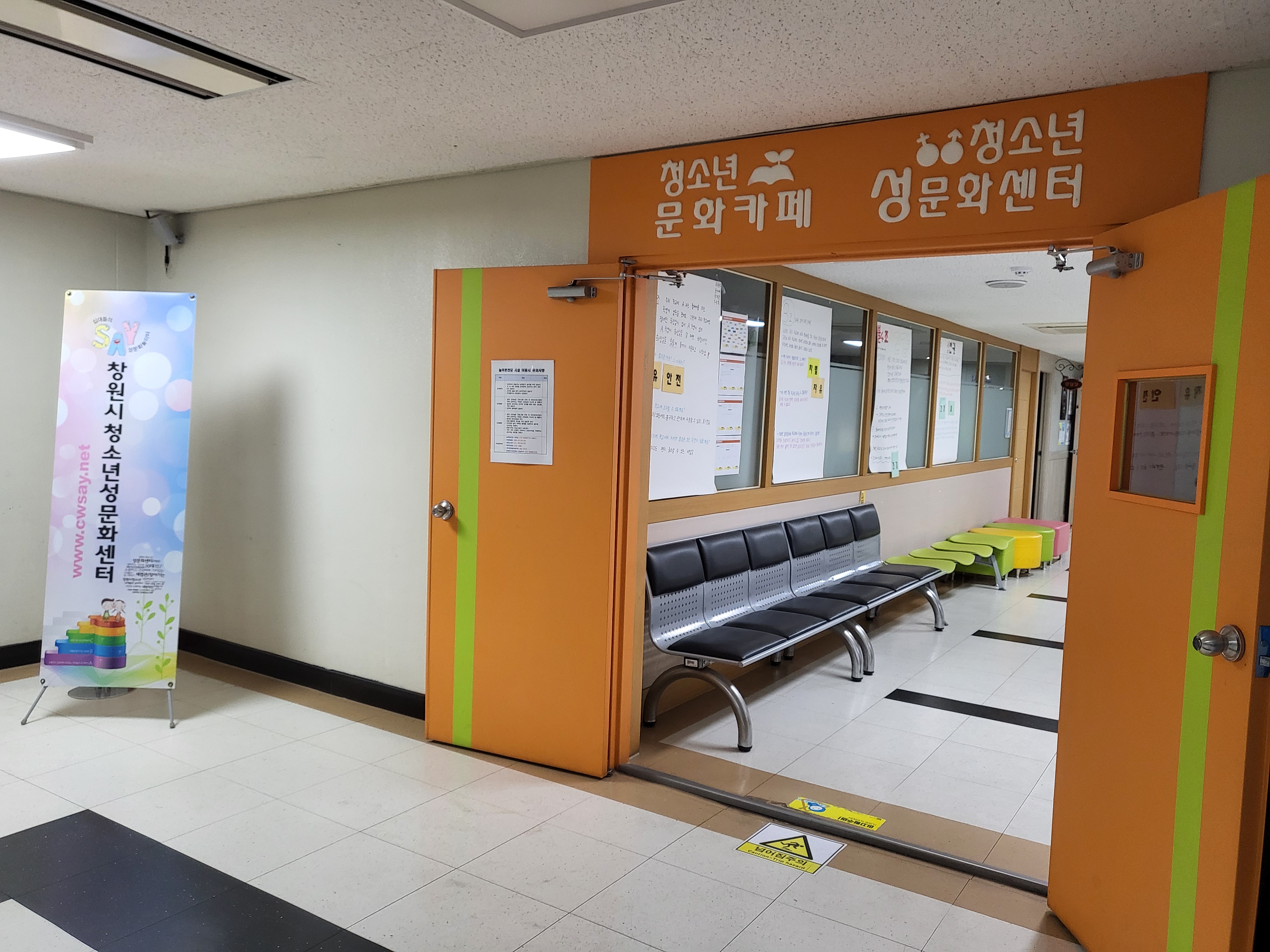 로비 우측에서 바라본 늘푸른전당의 청소년 성문화센터 입구이며, 입구 좌측에는 ‘창원시청소년성문화센터’라는 배너(현수막)가 세워져있다.