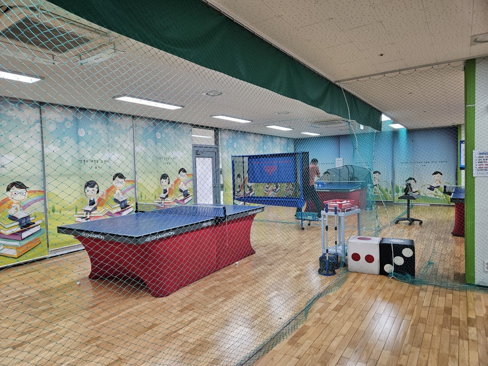 진동종합복지관 본관 2층 탁구장 전체적인 모습 촬영이며, 탁구대 2대 및 회원들이 탁구를 치고 있는 모습입니다.