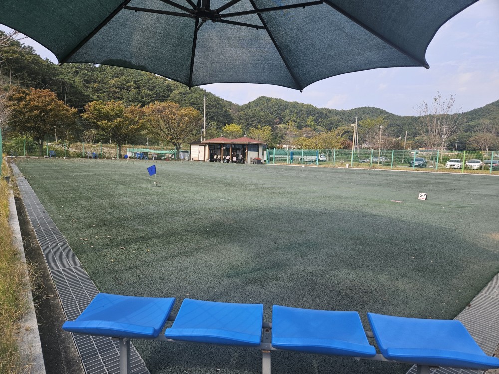 파라솔 아래 휴식의자에서 진동종합복지관 그라운드 골프장 가장자리에서 골프장을 촬영한 모습입니다