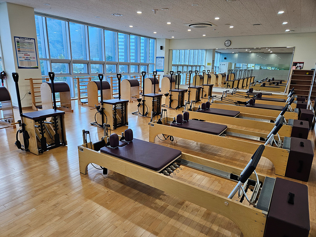 내부에서 바라본 필라테스 스튜디오입니다. 필라테스 기구들이 일렬로 놓여있고, 측면 벽에는 거울이 비치되어 있습니다.