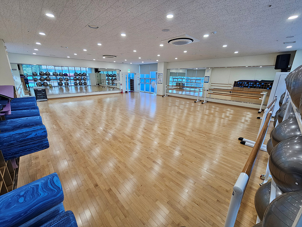 가장자리에서 바라본 다목적실 내부이며, 입구 포함하여 내부 전체가 보입니다. 양 방향으로 요가 도구와 필라테스 도구 등이 벽 쪽에 비치되어 있습니다.